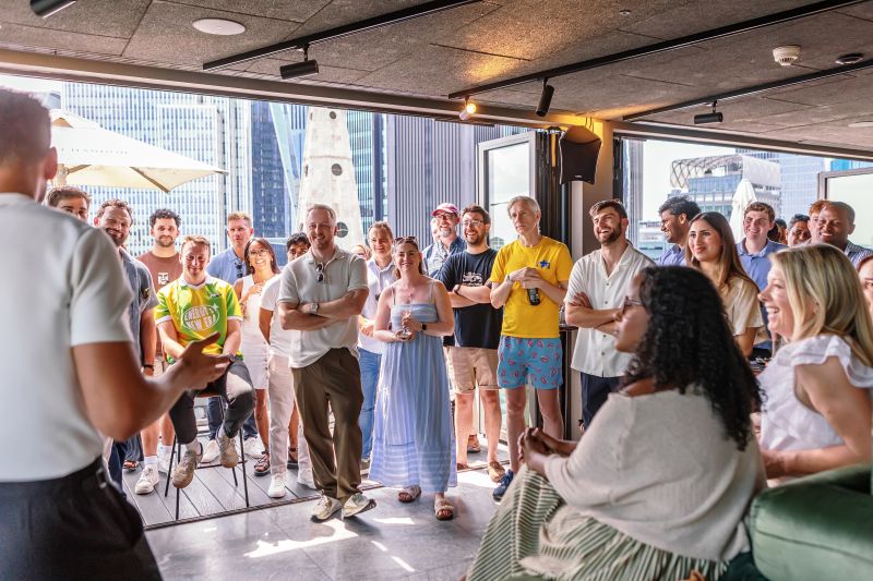 Guests listening to a speaker at a rooftop event with city views.