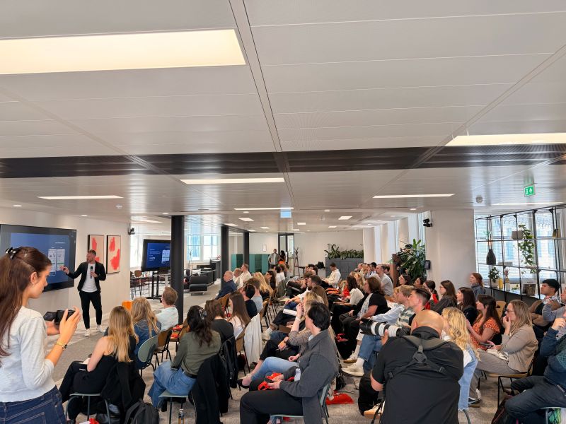 Speaker presenting to a seated audience in a bright office event space.