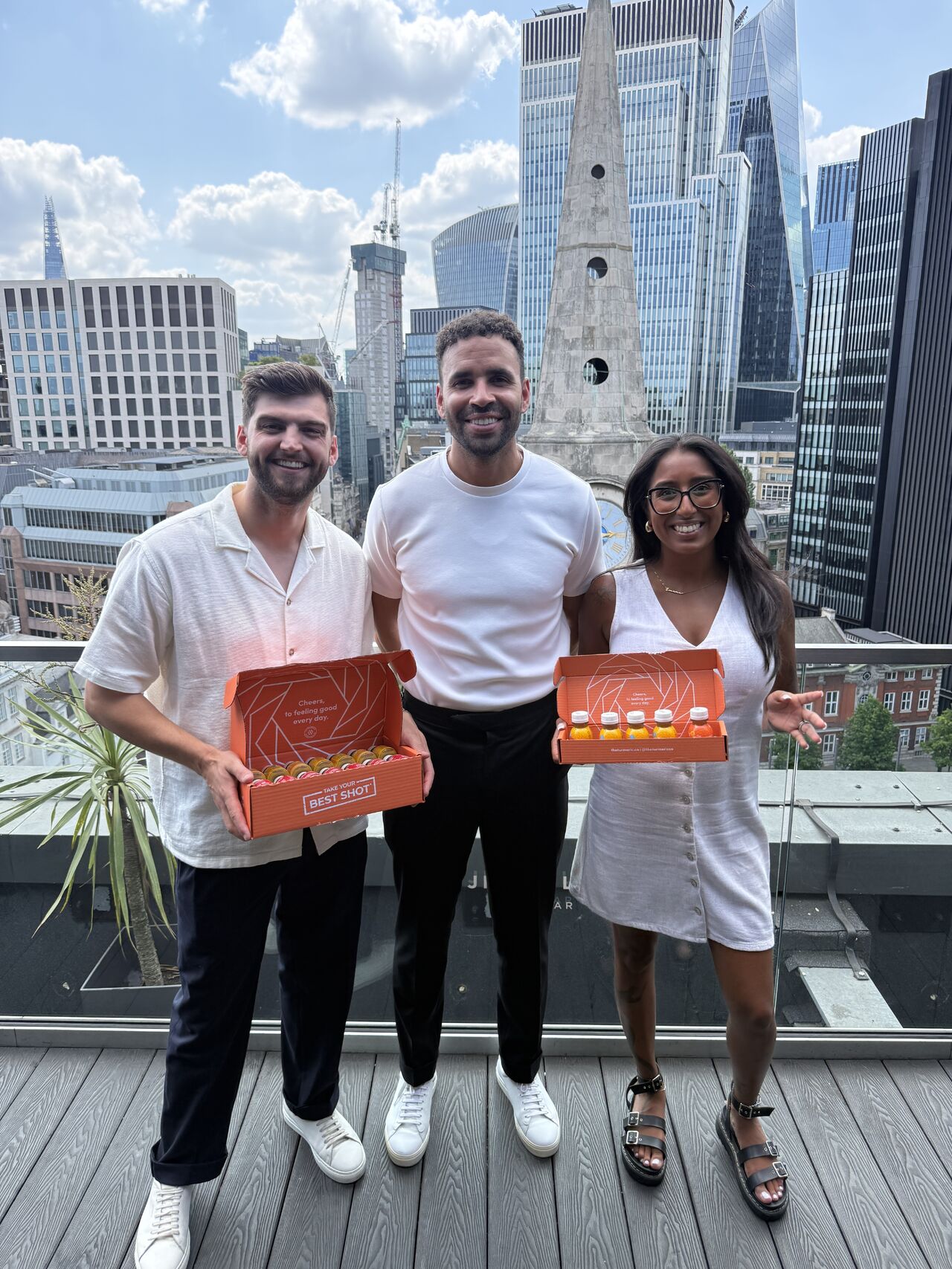 Three people holding The Turmeric Co. shot boxes on a city rooftop.